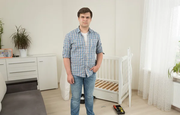 Portrait of young man posing against disassembled baby crib at n — Stock Photo, Image