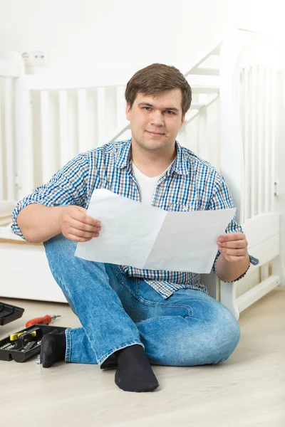 Mann sitzt auf dem Boden mit Anleitung zum Zusammenbau des Babybettes — Stockfoto