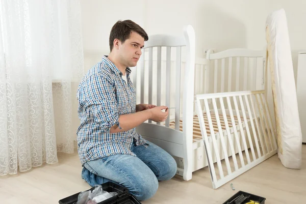 Homme assis sur le sol et réparant le lit de l'enfant dans la crèche — Photo