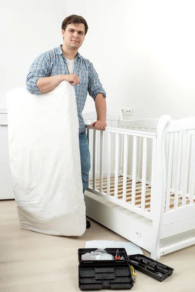 Glimlachende man die met matras bij gedemonteerde babybed — Stockfoto