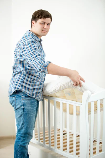 Expectant father putting mattress in baby's cot at nursery — Stock Photo, Image