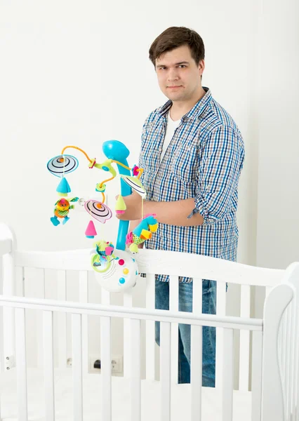 Porträt eines Mannes, der ein Spielzeugkarussell in seinem Babybett anbringt — Stockfoto