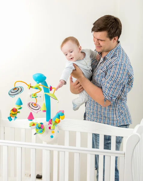 Jovem pai feliz mostrando novo carrossel de brinquedo no berço para seu bebê s — Fotografia de Stock