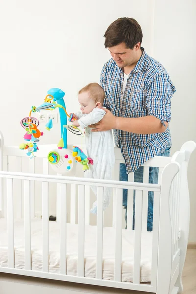 Sonriente padre sosteniendo a su lindo bebé en la cuna en la guardería —  Fotos de Stock