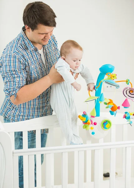 Young man taking his 9 months old baby son out of cot — Stock Photo, Image