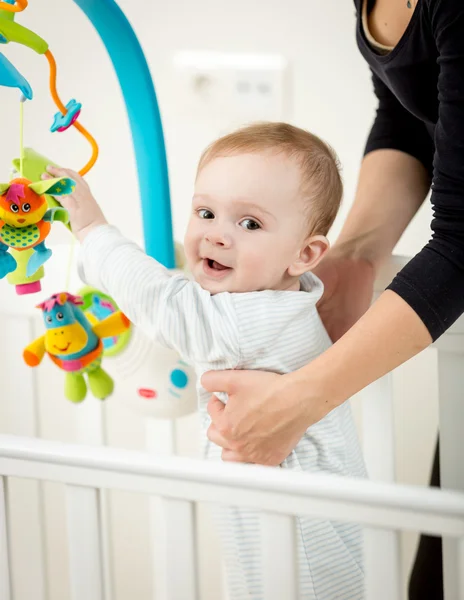 Porträtt av söt baby pojke leker med karusell i babysäng — Stockfoto