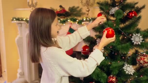 Portret van schattig meisje in trui kerstboom met kerstballen versieren — Stockvideo