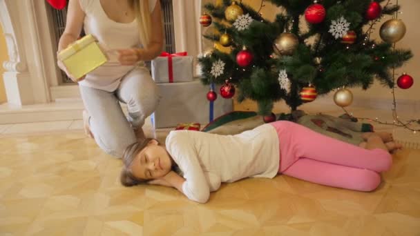 Mamma vaknar dottern som kändes somna under granen och ge hennes present. Glad flicka kramar mamma — Stockvideo