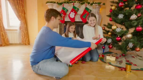 Gelukkige familie met meisje Kerstcadeaus inwikkeling in rood inpakpapier — Stockvideo