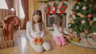 Noel ağacı ve açılış kutuları altında hediyelerle oturan pijama iki neşeli kız