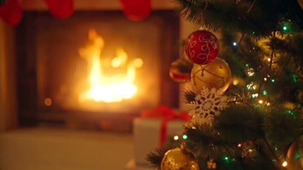 Fundo com bugigangas coloridas na árvore de Natal ao lado da lareira em chamas na sala de estar — Vídeo de Stock