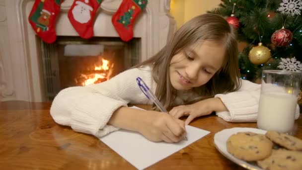 Dolly zastřelil roztomilé dívky v bílém svetru psaní dopisu Ježíškovi v obývacím pokoji u krbu — Stock video