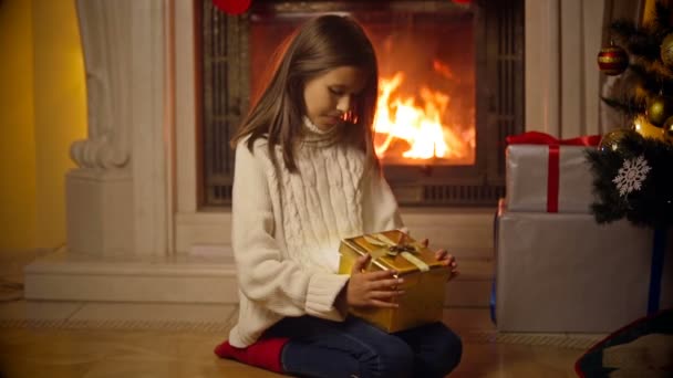 Χαριτωμένο κορίτσι σε πουλόβερ άνοιγμα μαγικό κουτί δώρου Χριστουγέννων. Φως και λάμψεις που φέρουν έξω από το κουτί — Αρχείο Βίντεο