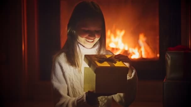 Retrato de menina animada olhando para dentro da caixa de presente de Natal. Pó mágico e luzes brilhantes voando para fora da caixa aberta — Vídeo de Stock