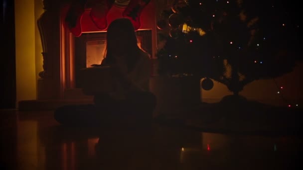 Dolly colpo di ragazza felice seduto sul pavimento al camino e scatola di apertura con regalo di Natale — Video Stock