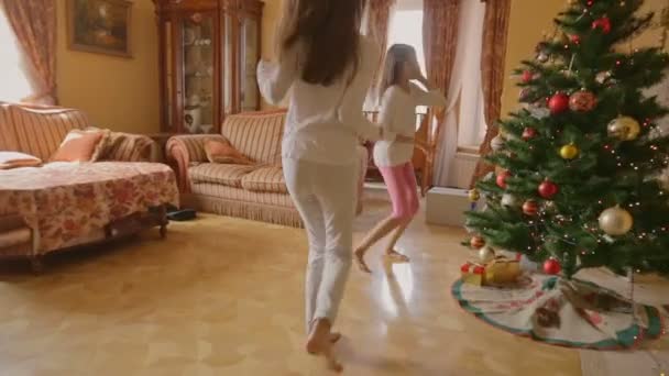 Duas meninas alegres em pijama correndo para presentes sob a árvore de Natal na manhã — Vídeo de Stock