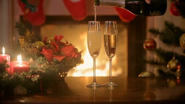 Наливаємо шампанське в дві склянки на різдвяний обідній стіл. Палаючий камін на фоні — стокове відео