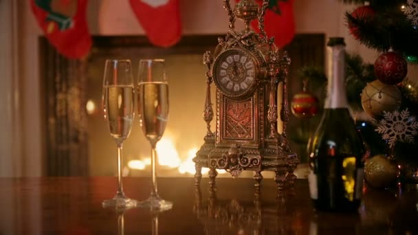 Dos copas de champán y reloj retro frente a la chimenea en casa. Concepto de celebrar la Navidad — Vídeos de Stock