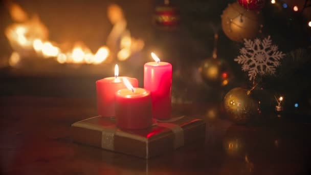Три палаючі червоні різдвяні свічки на обідньому столі у вітальні поруч з каміном та ялинкою — стокове відео