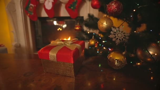 Dolly záběr červené Vánoční dárková krabice s zlatý luk na stole v obývacím pokoji s krbem — Stock video