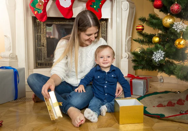 Pojke med sin mamma som öppna presentaskar under julgranen — Stockfoto