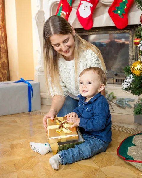 Sonriente madre y su hijo pequeño con regalo de Navidad en el suelo en —  Fotos de Stock