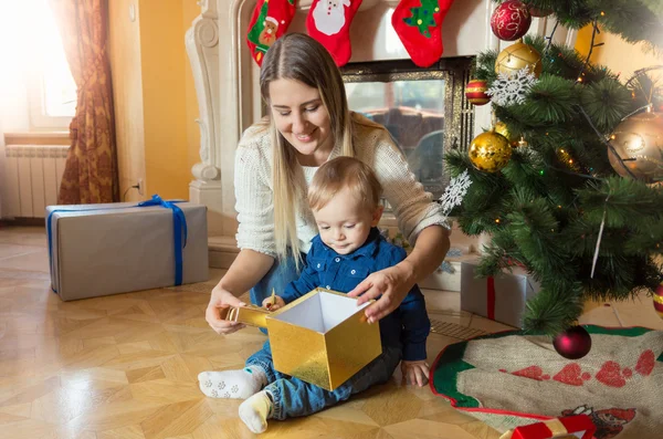 Mãe feliz com seu filho bebê sentado na árvore de Natal e loo — Fotografia de Stock