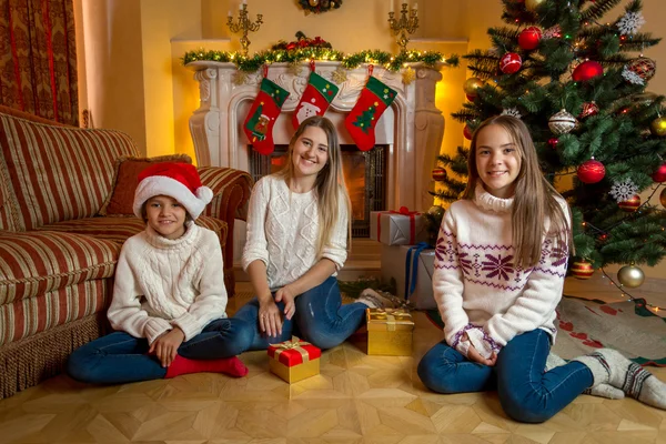 Zwei fröhliche Mädchen mit junger Mutter sitzen am Kamin in liv — Stockfoto