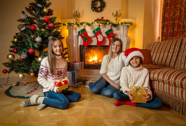 Happy young mother sitting with daughters on floor next to burni — Stock Photo, Image