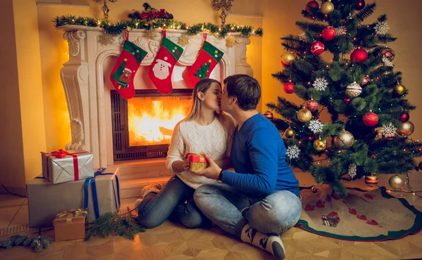 Jovem casal sentado na lareira e beijando no Natal e — Fotografia de Stock