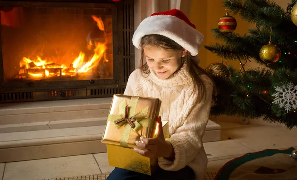Menina em Santa chapéu sentado na lareira ardente e olhando insid — Fotografia de Stock