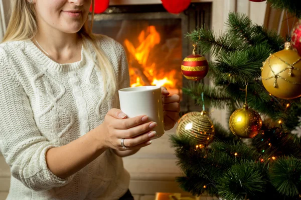 Frau sitzt am brennenden Kamin und schmückt Weihnachtsbaum — Stockfoto