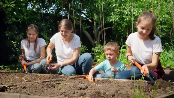 Grote familie met kinderen werken in huis achtertuin en graven grond op tuinbed om groenten te planten in het voorjaar — Stockvideo