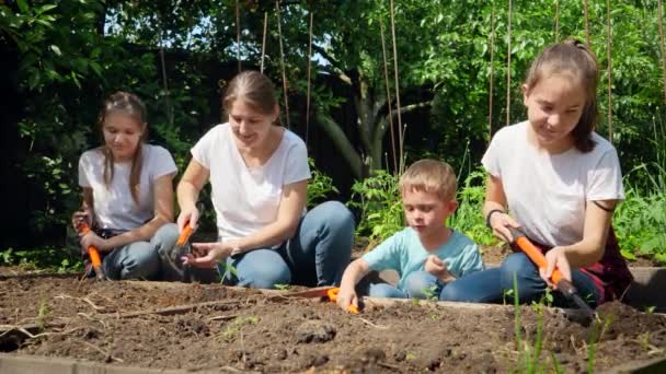 자녀들은 어머니가 정원에서 일하고 뒤 뜰에 있는 정원의 침대에 채소를 심도록 도와 줍니다. 협동과 가족이 함께 일 한다는 개념 — 비디오