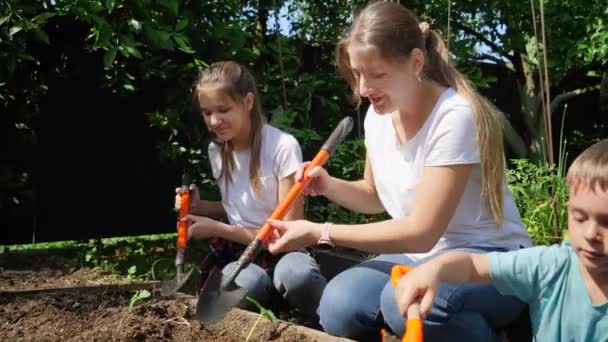 Långsam video av vuxna och barn som gräver jord i trädgården och planterar färska ekologiska plantor — Stockvideo