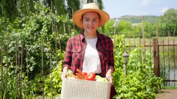 Χαμογελαστή γυναίκα σε καπελιέρα με ώριμα βιολογικά λαχανικά και περπάτημα στον κήπο. Έννοια των μικρών επιχειρήσεων και καλλιέργεια βιολογικών λαχανικών στον κήπο πίσω αυλή — Αρχείο Βίντεο