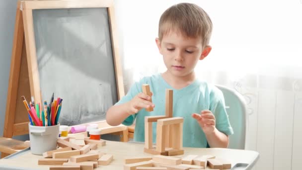 Portrét malého chlapce hrajícího si s dřevěnými tvárnicemi a stavební věží z cihel. Koncepce inteligentních dětí a domácí výchovy během uzamykání a vlastní izolace. — Stock video