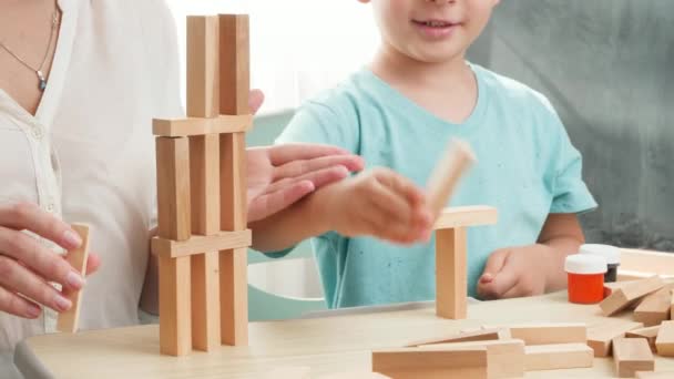 Smart boy with mother playing with wooden toy blocks and building high tower. Mother educating and teaching her child at home during lockdown and self isolation — Stock Video