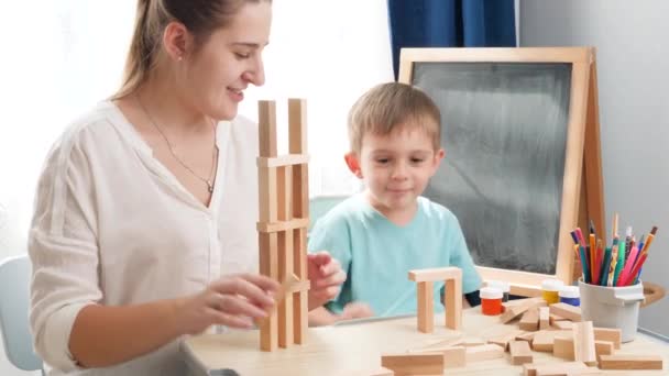 Ragazzino con la madre che ride dopo alta torre di blocchi di legno giocattolo cadere. Madre educare e insegnare il suo bambino a casa durante l'isolamento e l'autoisolamento. Famiglia divertendosi — Video Stock