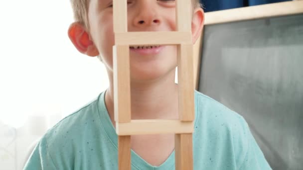 Glad skrattar och ler pojke tittar genom höga trä torn gjorda av block och tegel. Begreppet utbildning för barn i hemmet under inlåsning och vistelse i hemmet — Stockvideo