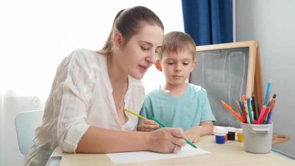 Usmívající se mladá matka kreslí obrázek se svým malým synem tužkami. Pojem rodičovství a vzdělávání doma. Kreativita a dětské umění — Stock video