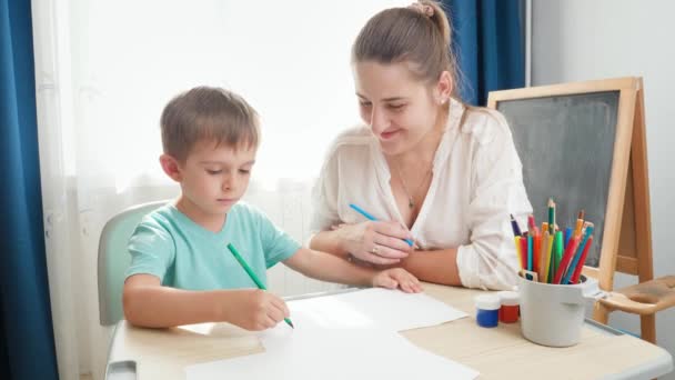 Madre joven mirando a su pequeño hijo dibujando o escribiendo. Aprendizaje infantil dibujar o escribir en casa durante el aislamiento y el encierro — Vídeos de Stock