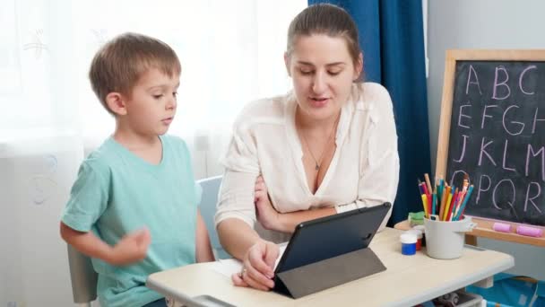 Ung kvinnlig lärare med liten pojke som använder surfplatta dator medan du lär dig alfabetet i klassrummet. Föräldra- och distansutbildning i hemmet. — Stockvideo