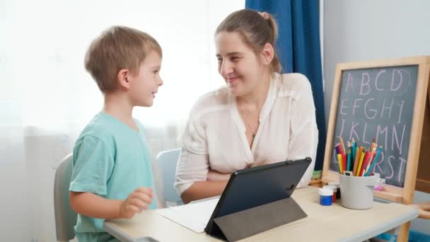 Chlapec studuje doma na digitálním tabletu. Matka se dívá na svého syna, jak dělá domácí úkoly na počítači tabletu — Stock video