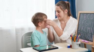 Gözlüklü küçük çocuk annesiyle tablet bilgisayarında oynuyor. Uzun süre alet ve bilgisayar kullandıktan sonra çocukların görme ve görme sorunları oluyor..