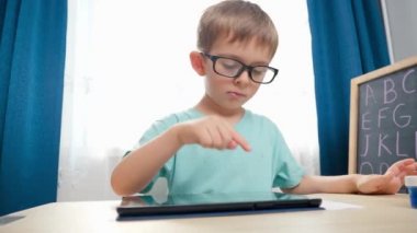 Tablet bilgisayarında oynayan ve ders çalışan gözlüklü zeki çocuk portresi. CHild ödev yapmak için aygıt kullanıyor.