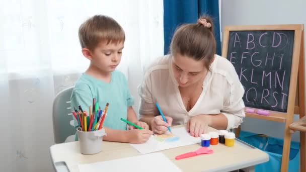 Menino pequeno com mãe jovem desenho e pintura com lápis coloridos. Fazendo lição de casa e edcucação com os pais. — Vídeo de Stock