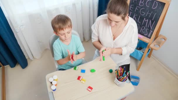 Top ver video de niño con la madre dando forma y escultura de plastilina de colores y arcilla. Familia divirtiéndose con colorida masa de juguete — Vídeo de stock