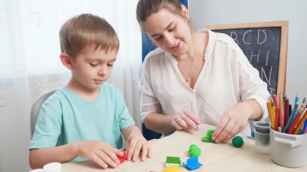 Usmívající se matka učí svého malého syna modelovat a tvarovat tvary s barevnou hlínou nebo plasticínem. Rodinné hraní s hračkou těsto pro tvarování — Stock video