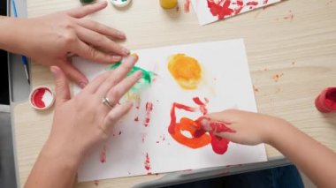 Annesi resim çizen ve elleri beyaz kağıda renkli boya bulaşmış küçük bir çocuk. Çocuk eğitimi, yaratıcılık gelişimi ve sanat kavramı.